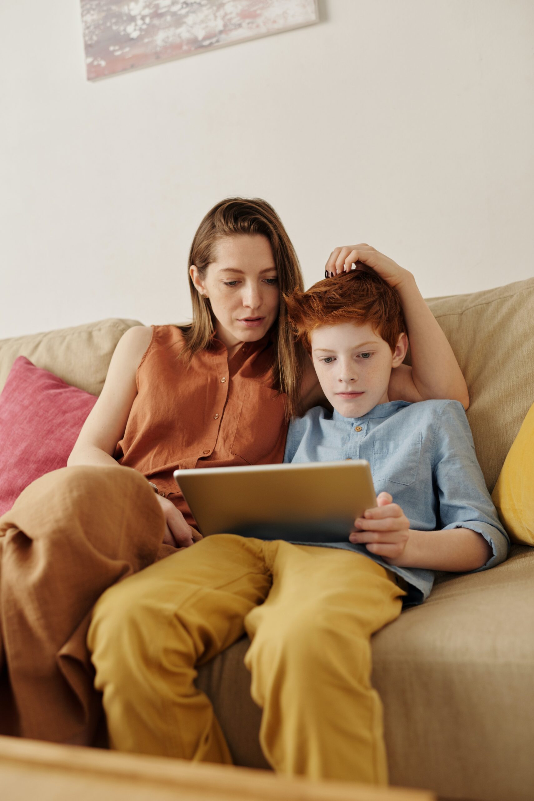 An adult sits by a child using an ipad as part of speech therapy AAC